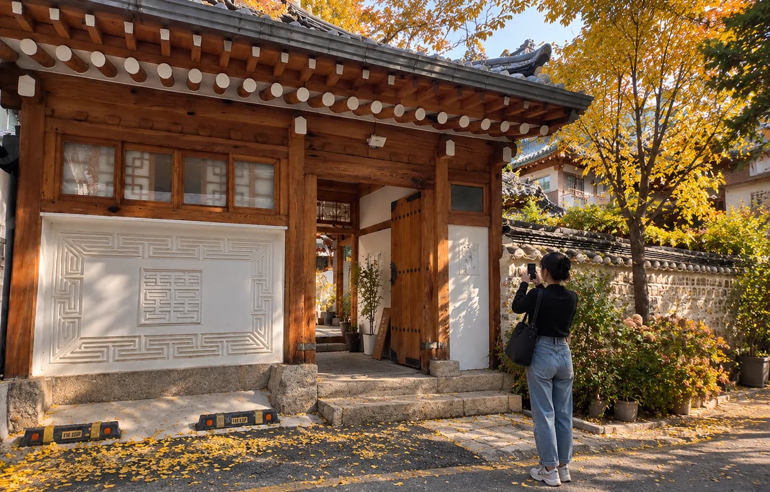 A visitor photographing a hanok gate in Seochon with fallen ginkgo leaves on the ground