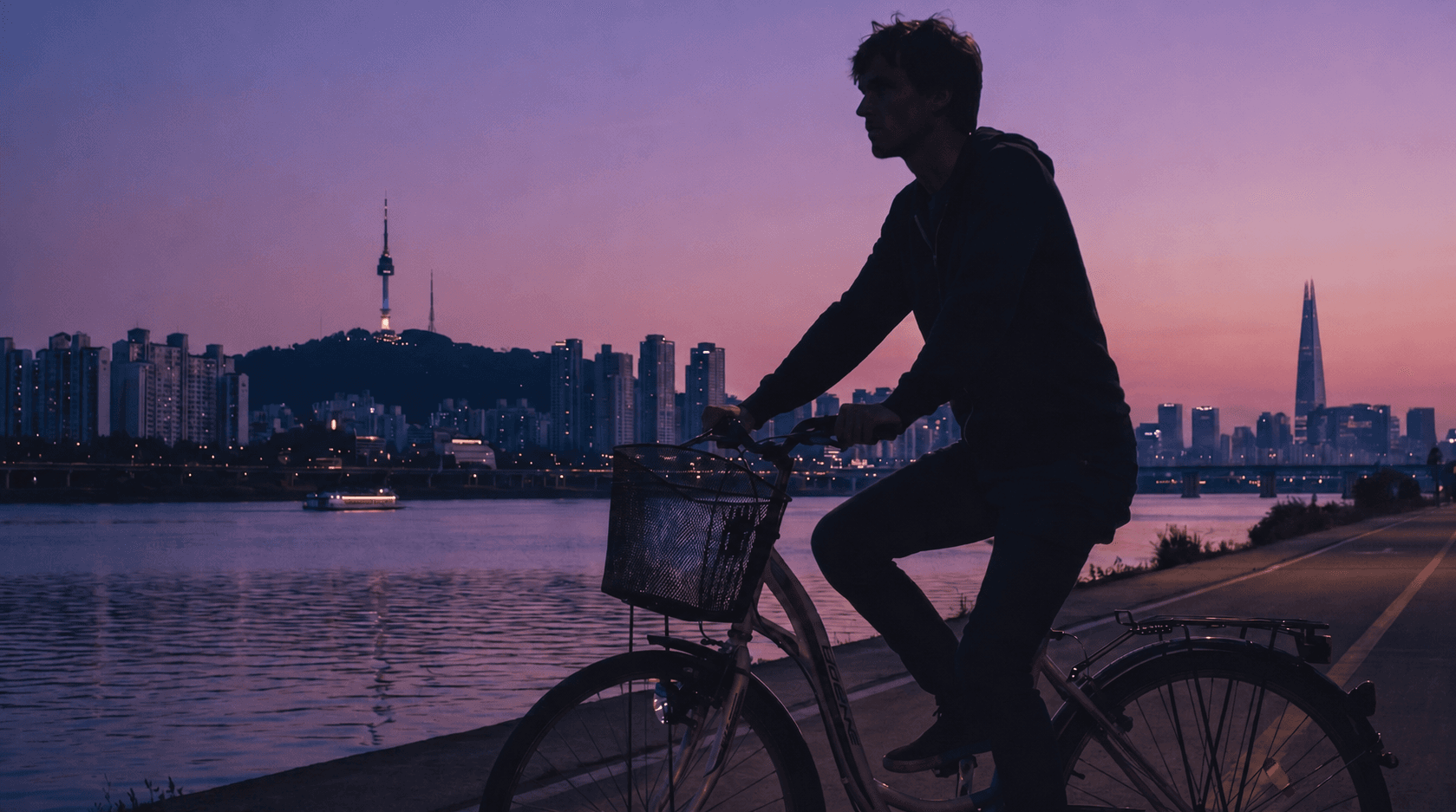 Cyclist riding along the Han River at dusk with the Seoul skyline and N Seoul Tower